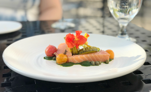 An appetizer of cold-smoked salmon with a vibrant garlic and tarragon puree, blistered cherry tomatoes, capers and sweet pickles.