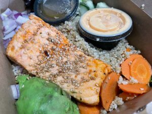 Sriracha poké bowl: A generous piece of seared salmon glazed with greens, quinoa, onion, avocado and pickled carrots. Sesame seeds are sprinkled throughout and there are just enough leaves of cilantro for added flavor.